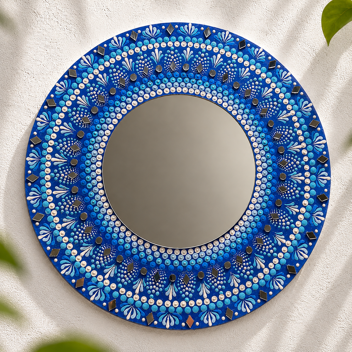 Round 12-inch wall mirror with a hand-painted blue mandala frame featuring cobalt, turquoise and pearl dot art patterns with small inlaid diamond mirror tiles on a white wall
